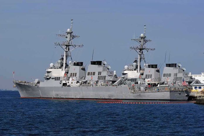 Three gray naval destroyers docked side by side at a pier