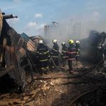 Firefighters amid twisted metal and smoke at a disaster site