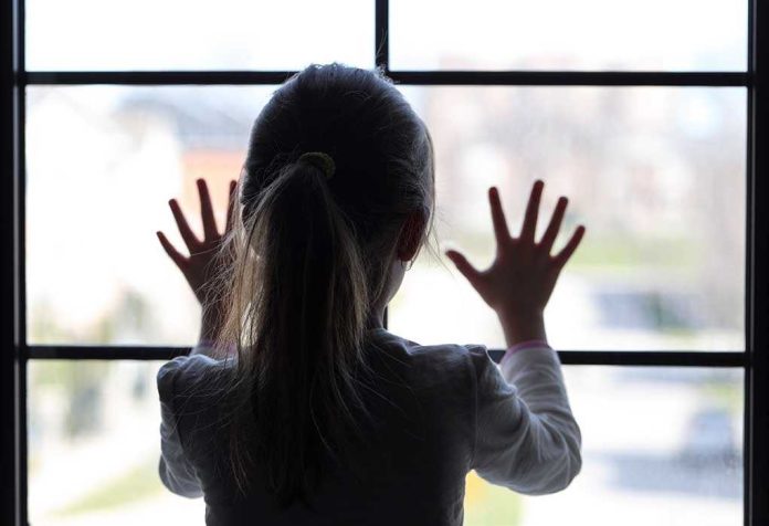 shutterstock_189988664 A child with long hair presses their hands against a window, looking outside