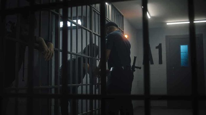 shutterstock_2438057445 police officer at a jail cell with detainees behind bars