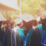 Graduates in caps and gowns walking at an outdoor ceremony
