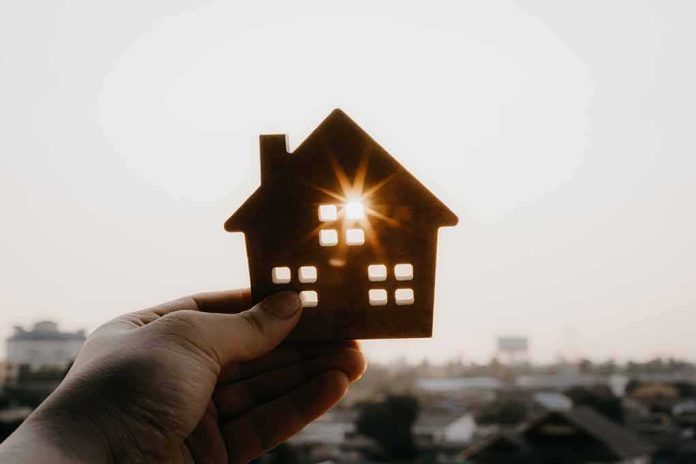 shutterstock_1043134735 Hand holding a small house cutout against a bright sunset sky
