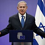 Shock War Cry Shakes Israel’s Cabinet man in suit speaking at a podium with Israeli flag