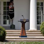 Unlikely Alliance Forms — Hollywood Tax Fight Podium with presidential seal in a garden colonnade