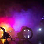 ICE Expands Less-Lethal Arsenal Handcuffs on a surface with police cars and flashing lights in smoky darkness