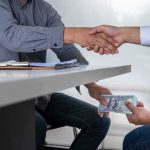 Top Watchdog’s Lover Twist—$1.2M Flows Two people shake hands over a desk while cash is exchanged underneath