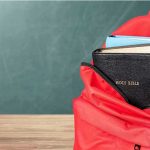 Mandatory Bible Lessons: What Gets Cut? Red backpack with books on a classroom desk