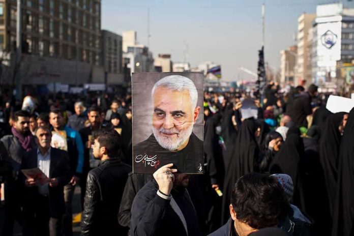 shutterstock_1609234762 Qasem Soleimani portrait held aloft in a crowded street gathering