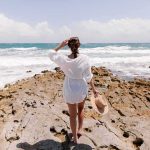 Families Stunned by Toxic Beach Crawler Woman in white cover-up standing on rocky shore by the ocean