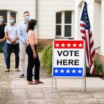 Nine Felonies: Voter Scam Stuns City Voters wearing masks line up outside a polling place