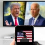 Progressive Brand Bulldozes Age Attack Smartphone with ballot icon held before a TV showing two blurred politicians