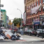 Street Fight Becomes Child’s Funeral Street corner with piled garbage bags and traffic near brick storefronts