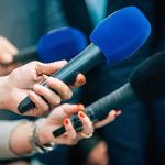 Navy Bottleneck Sidelines 100,000-Ton Giant Reporters holding colorful microphones