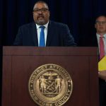 Another Nightclub Burns — Promises Burned Too Man speaks at podium with New York County District Attorney seal