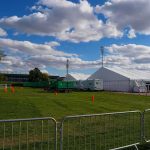 Patriots: Watch the Games — And Watch the Rulebook Around Them Temporary white tents and equipment on a grassy field with traffic cones and metal barriers