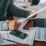 Questions Swirl Over Cambridge Professor Person reviewing bills with calculator at cluttered desk