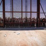 Security Clampdown Hits Palestinian Workers Crowd stands behind tall metal fence at border crossing