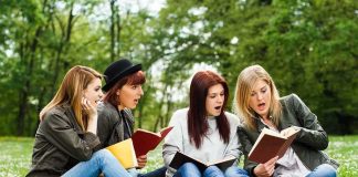 Group of young women reading books on grass in a park