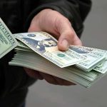 A $35 Million Investment Scheme Finally Collapsed A hand holding a stack of hundred dollar bills with one bill prominently displayed