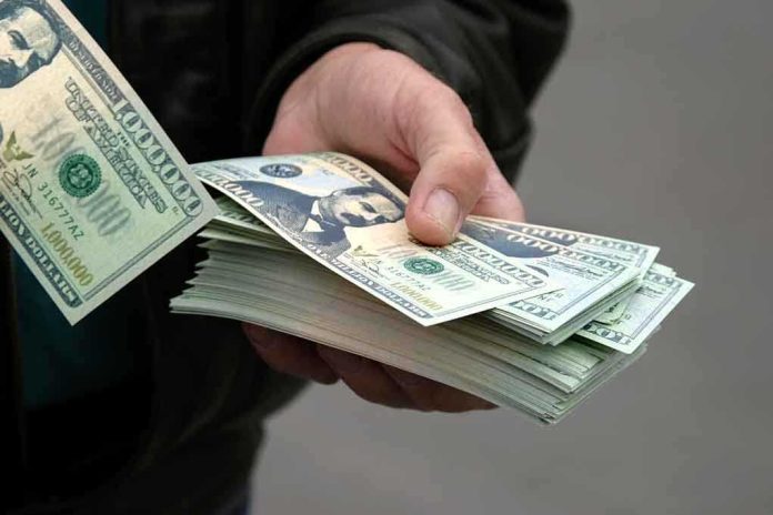A hand holding a stack of hundred dollar bills with one bill prominently displayed