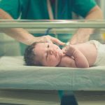 Newborn baby in hospital bassinet being cared for by nurse
