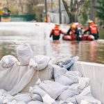 Flood Chaos: Shocking Indiana Rescue Video Exposes Gaps Sandbags stacked near a flooded street with rescue workers in a boat