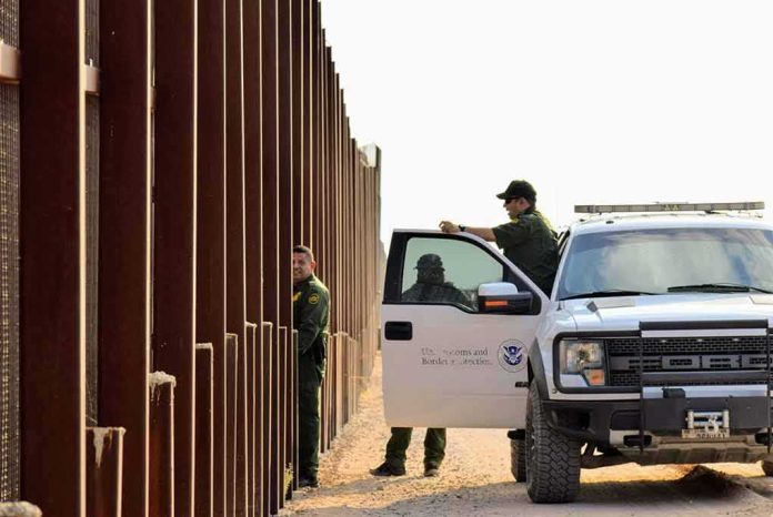 shutterstock_1545833798 Border patrol agents near a tall fence and a marked pickup truck