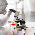 Scientist in protective gear using a microscope at a lab bench