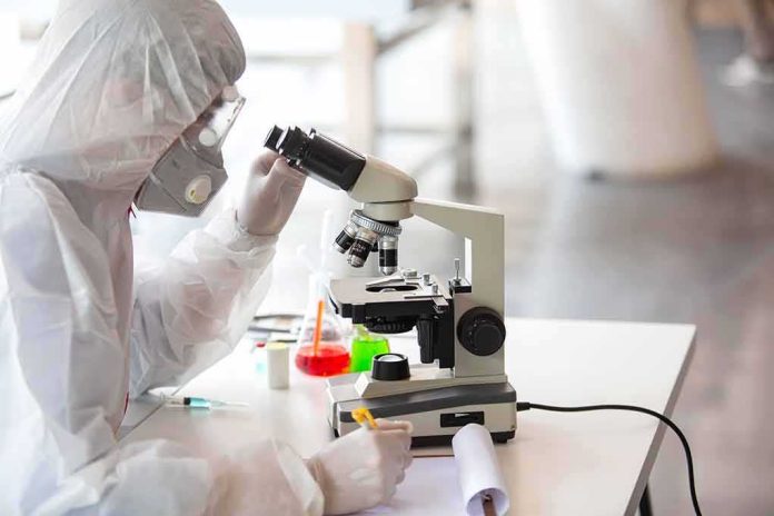 Scientist in protective gear using a microscope at a lab bench