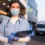Plague Panic Whispered, Quarantines Explode Healthcare worker in scrubs wearing mask and gloves holding a clipboard
