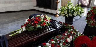 Coffin Shock: Dead Girl Starts Talking Coffin with floral arrangements at a funeral service