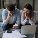 They Were Found Dead Outside Their $12M Home Couple on couch stressed while reviewing bills and laptop