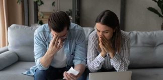They Were Found Dead Outside Their $12M Home Couple on couch stressed while reviewing bills and laptop