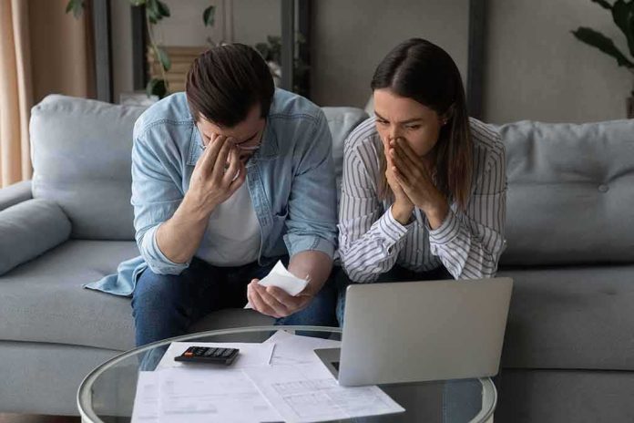 shutterstock_1916669321 Couple on couch stressed while reviewing bills and laptop