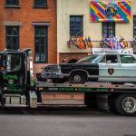 Tow truck carrying vintage sheriff car on city street