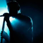 Shock Move: Free Palestine Hits Gillette Singer silhouette holding a microphone on a dark stage