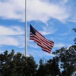 Wildfire Guts Homes – One Flag Defies It American flag at half-staff against a blue sky