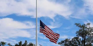 American flag at half-staff against a blue sky